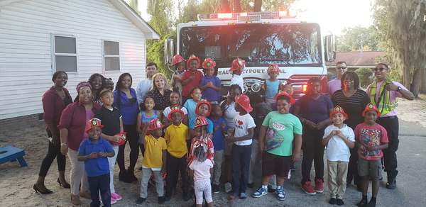 Group photo of kids with fireman hats in front of firetruck