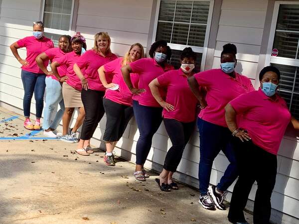 9 women posing next to building in pink shirts